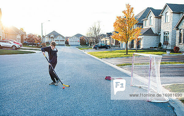Jugendlicher  der allein in einer Wohnstraße Streethockey spielt.