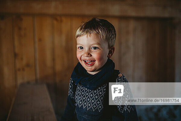 Liebenswerter Junge lächelt in einer Holzhütte im Winter