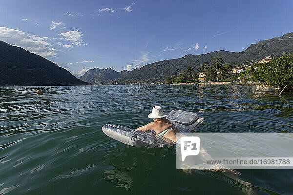 Eine weibliche Sonnenanbeterin schwimmt auf einem Floß im Iseosee  Italien