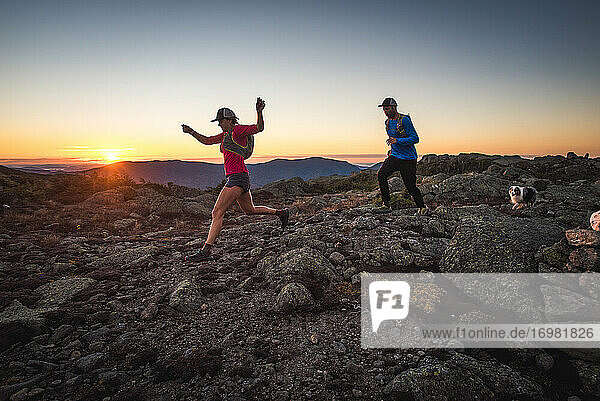 Mann und Frau beim Trailrunning mit Hund in den Bergen bei Sonnenaufgang