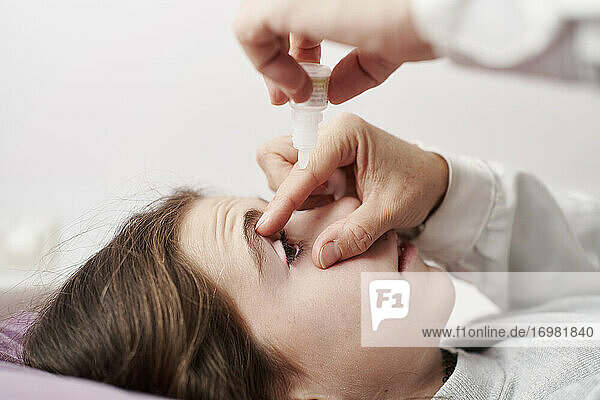 Detail of female doctor smiling and giving eye drops to a little girl in her bed. Home doctor concept