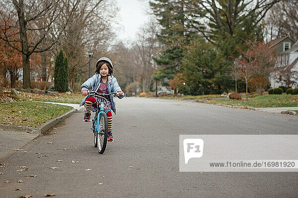 Ein kleines Mädchen in gestreiften Strumpfhosen und mit Helm fährt allein die Straße entlang