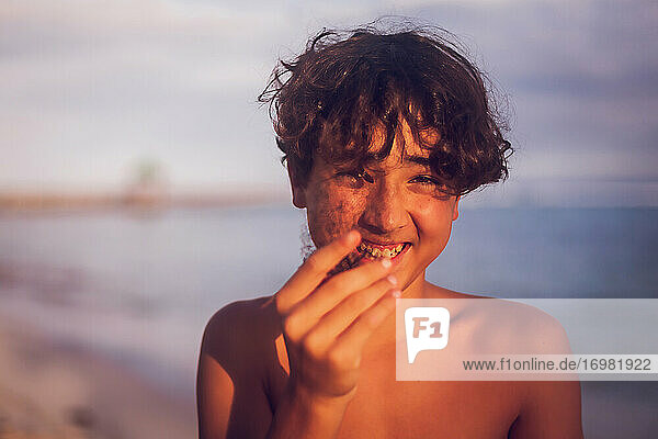 Smiling pre teen boy holding a coral on a tropical beach.
