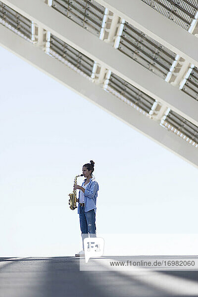 Woman with ponytail playing a saxophone while standing outdoors