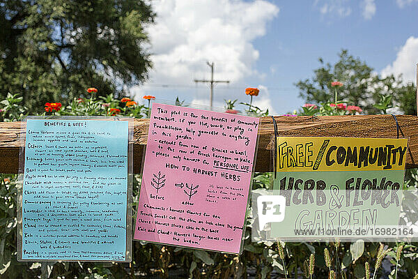 Bunte Schilder am Zaun eines Gemeinschaftsgartens vor einem strahlend blauen Himmel