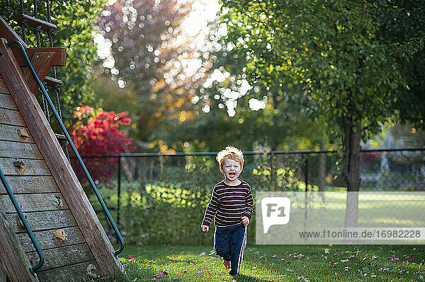 Caucasian männlich 3-4 Jahre alt läuft im Gras im Hinterhof lächelnd