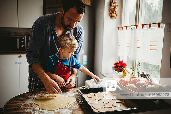 Vater und Sohn in der Küche zu Hause beim Backen von Weihnachtsplätzchen im Pyjama
