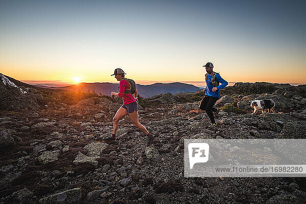 Man and woman trail running with dog in mountains at sunrise