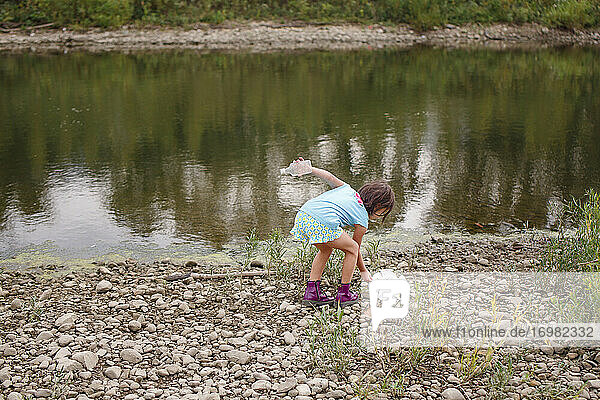 A little girl cleans litter up off of the shoreline of a river
