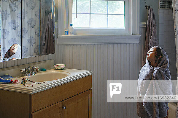 Ein kleines Mädchen  eingewickelt in ein Badetuch  starrt auf ihr Spiegelbild