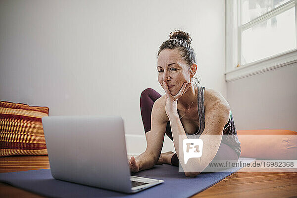 Frau bereitet sich darauf vor  in ihrer Wohnung mit einem Laptop Yoga zu üben