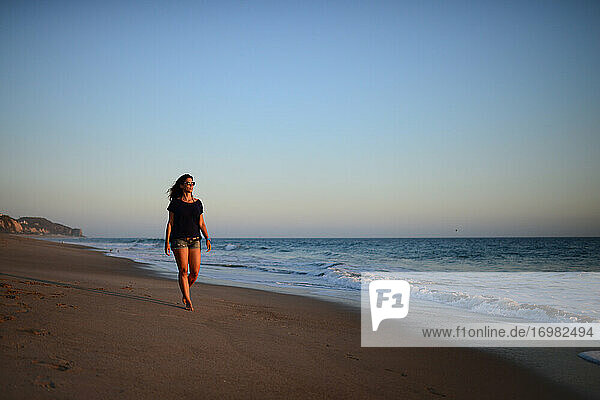 Junge Frau geht bei Sonnenuntergang am Strand spazieren