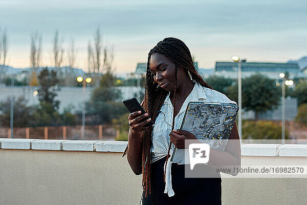 Junge Studentin mit schwarzer Hautfarbe schaut auf einem Campus auf ihr Handy