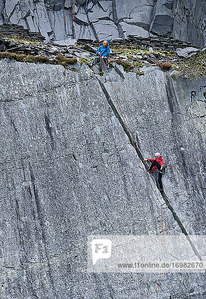 Frau klettert in einem Schiefersteinbruch in Nordwales eine steile Felswand hinauf