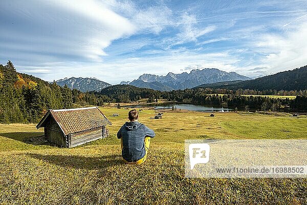 Junger Mann sitzt in der Wiese  Heustadl auf Wiese am Geroldsee  Gerold  Blick auf Karwendelgebirge  Bayern  Deutschland  Europa