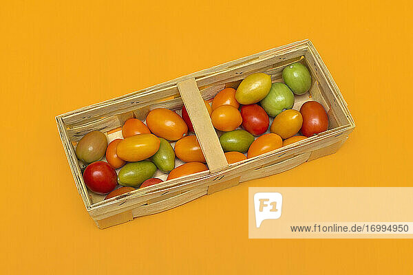 Frische Multicolor-Kirschtomaten in Kiste auf orangem Hintergrund