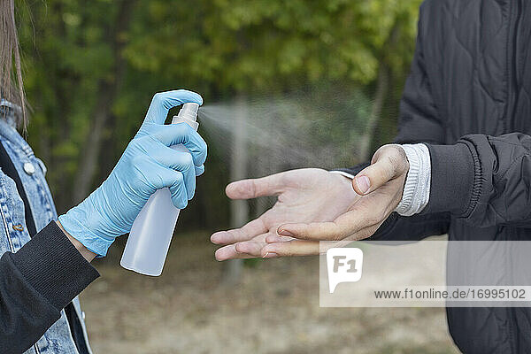 Close up Frau in Schutzhandschuhen sprühen Freund mit Hand Desinfektionsmittel