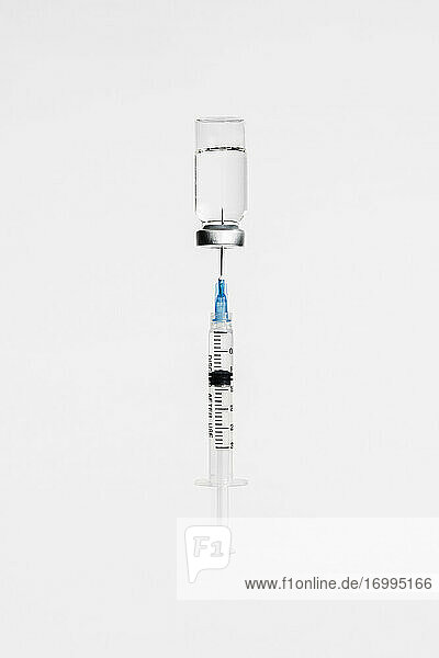 Syringe in COVID-19 vaccine vial on white background