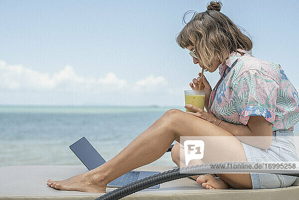 Frau schlürfen Cocktail am Laptop am Strand Liegestuhl