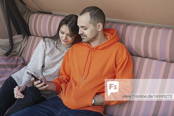 Junges Paar mit Smartphone auf der Terrassenschaukel