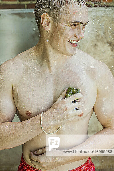 Glücklicher junger Mann mit Seife beim Duschen im Freien