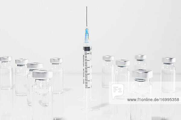 COVID-19-Impfstoff-Ampullen  die eine Spritze umgeben  auf weißem Hintergrund