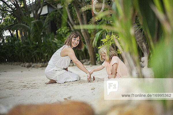 Portrait glückliche Mutter spielt mit Tochter im Sand am tropischen Strand