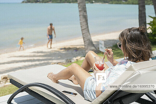 Woman enjoying cocktail on sunny beach lounge chair