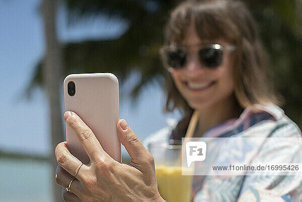 Glückliche Frau mit Cocktail nehmen Selfie am sonnigen Strand