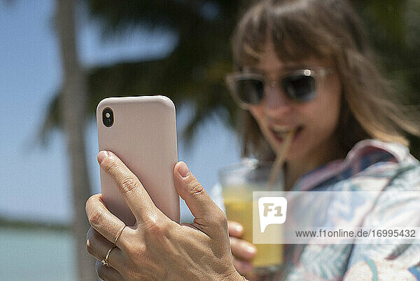 Frau mit Smartphone schlürfen Cocktail am sonnigen Strand