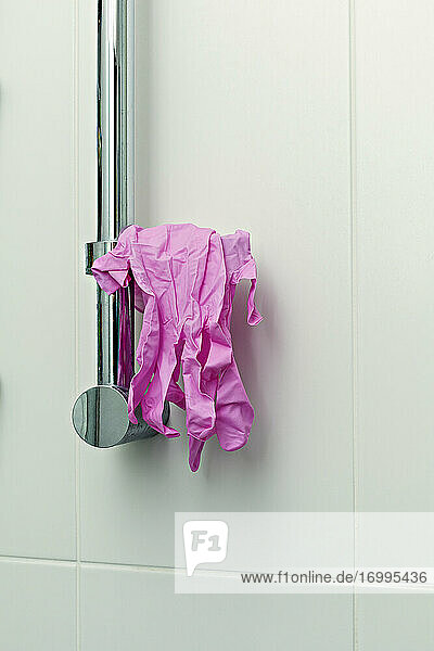 Rosa Schutzhandschuhe hängen am Duschgriff