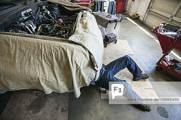 Mechaniker liegt auf einem Wagen unter einem Auto in einer Autowerkstatt
