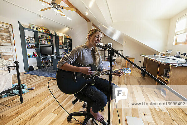 Fourteen year old teenage girl playing her guitar and singing at home in loft space