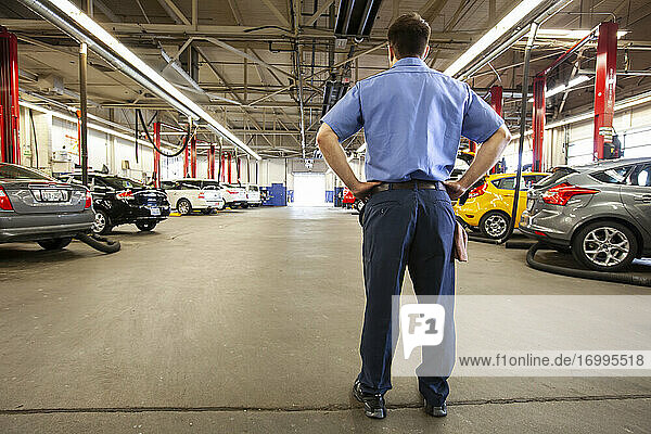Auto mechanic in a repair shop  rear view man with hands on hips