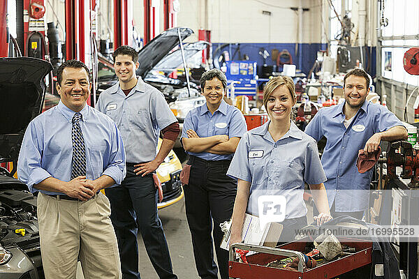 Portrait of smiling auto repair shop team with Hispanic male owner