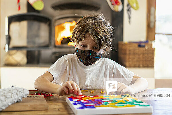 young boy wearing mask playing board game at home