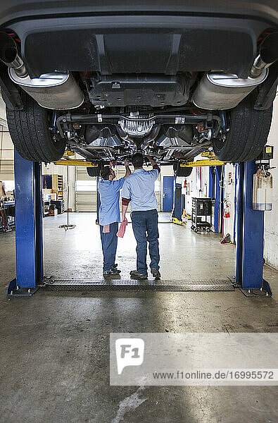 Zwei Mechaniker arbeiten auf einer Hebebühne in einer Reparaturwerkstatt an der Unterseite eines Fahrzeugs
