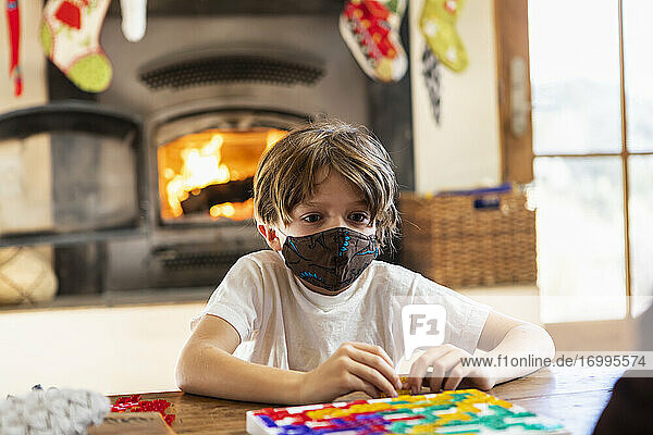 young boy wearing mask playing board game at home