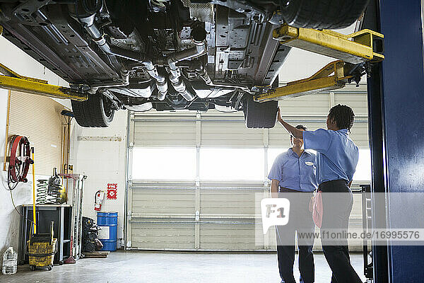 Zwei Mechanikerinnen arbeiten auf einer Hebebühne in einer Reparaturwerkstatt an der Unterseite eines Fahrzeugs