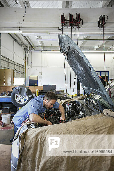 Ein Mechaniker in einer Autowerkstatt lehnt sich in den Motor eines Autos  an dem er gerade arbeitet