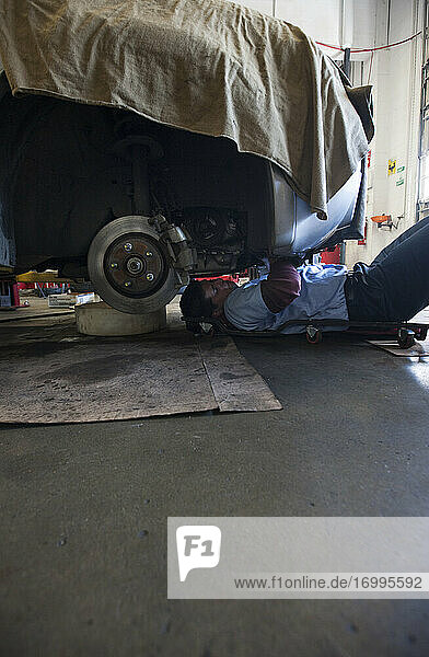 Mechaniker liegt auf einem Wagen unter einem Auto in einer Autowerkstatt