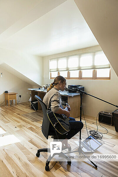 Fourteen year old teenage girl playing her guitar and singing at home in loft space
