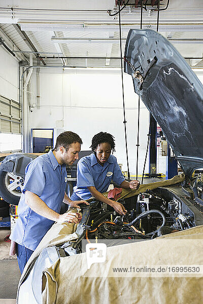 Male and female mechanics talk as they look at engine in auto repair shop