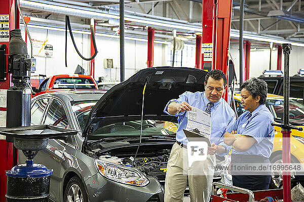 Owner of auto repair shop talks with Hispanic female mechanic