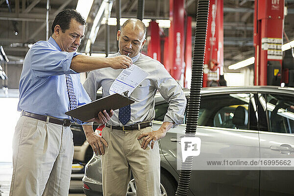 Male Hispanic owner of auto repair shop talking to a male Pacific Islander manager in the shop