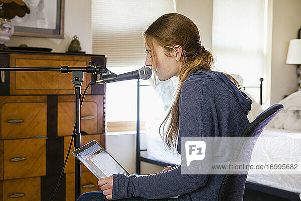 Teenage girl singing into a microphone in her bedroom