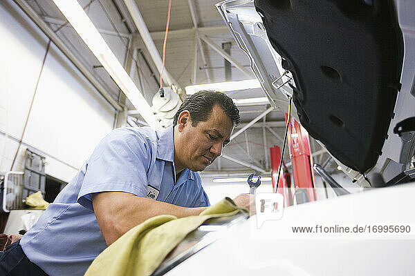 Ein hispanischer Mechaniker lehnt sich in den Motor eines Autos  an dem er in einer Autowerkstatt arbeitet