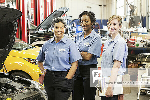 Porträt von drei lächelnden Mechanikerinnen in einer Autowerkstatt