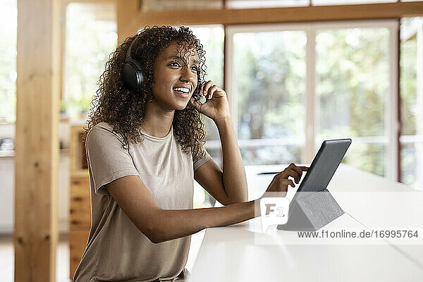 Geschäftsfrau mit digitalem Tablet  die über Kopfhörer spricht  während sie zu Hause sitzt