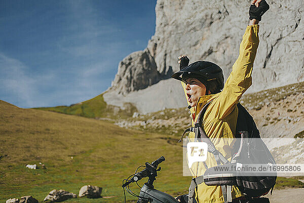 Aufgeregte Radfahrerin mit erhobenen Armen  die im Nationalpark Picos de Europa an einem sonnigen Tag schreit  Kantabrien  Spanien